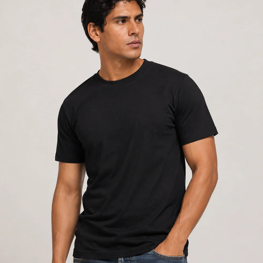 A man wearing a plain black short-sleeve crewneck t-shirt and blue jeans, standing against a light gray studio background.
