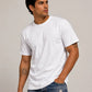 A man wearing a plain white short-sleeve crewneck t-shirt and distressed blue jeans, standing against a neutral light gray studio background.