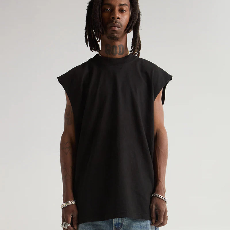 Man wearing a black sleeveless shirt and jeans against a plain background